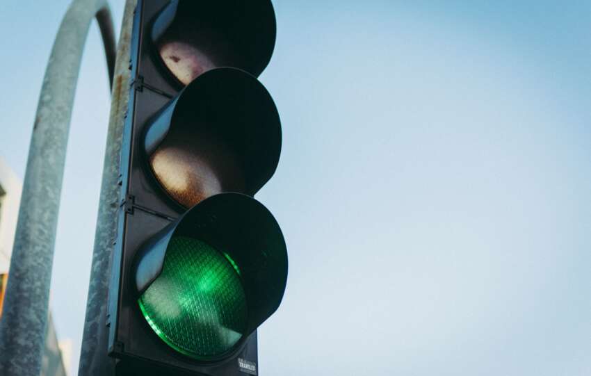 Close-up of a green traffic light against a clear blue sky, symbolizing go and safety.