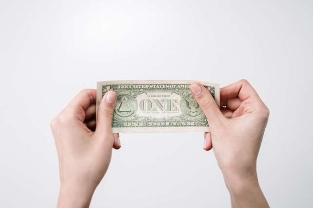 A close-up image of hands holding a one dollar bill, symbolizing finance and economy.