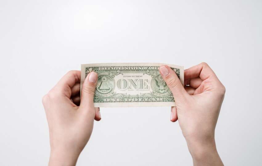 A close-up image of hands holding a one dollar bill, symbolizing finance and economy.