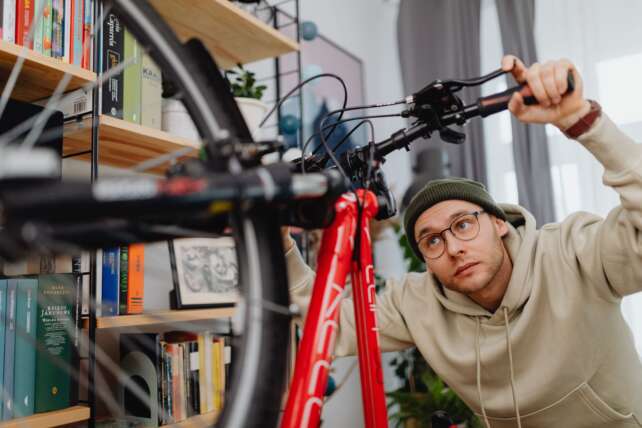 A man focuses on repairing a bicycle indoors, surrounded by bookshelves and tools.