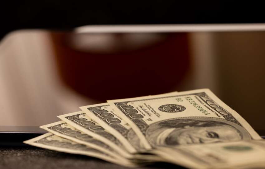 Close-up image of multiple dollar bills placed beside a laptop, symbolizing finance and digital economy.