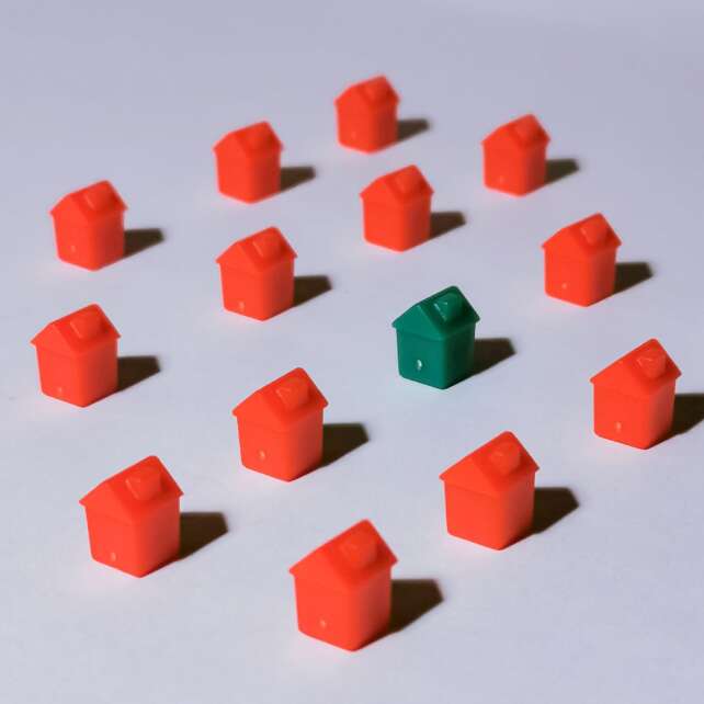 Miniature red and green monopoly houses on a white backdrop emphasizing contrast and arrangement.