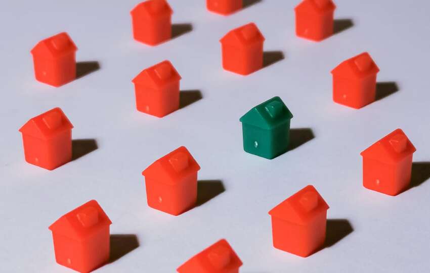Miniature red and green monopoly houses on a white backdrop emphasizing contrast and arrangement.