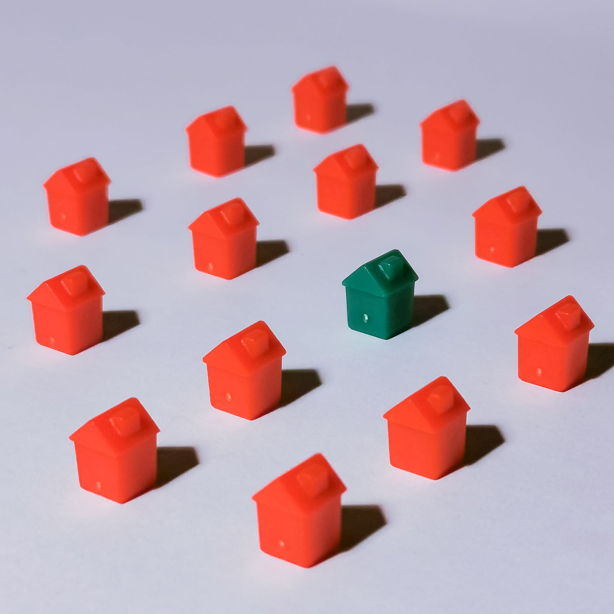 Miniature red and green monopoly houses on a white backdrop emphasizing contrast and arrangement.