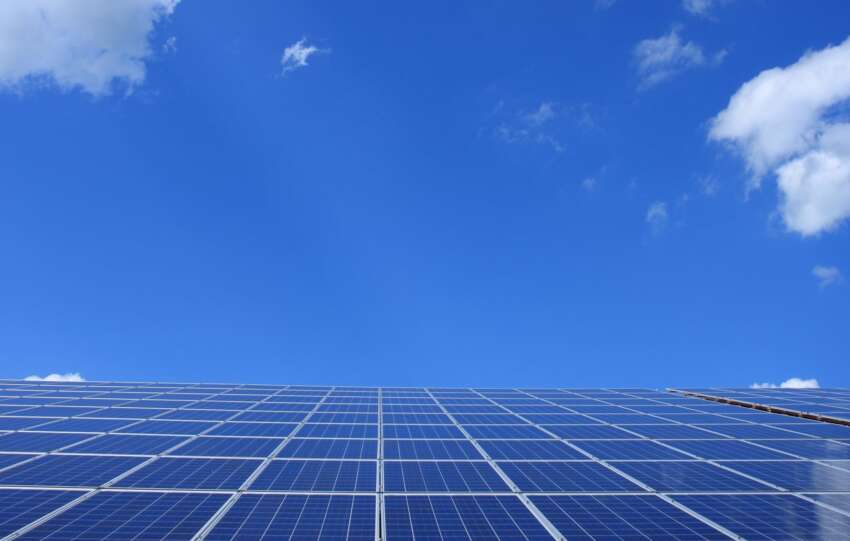 A low angle view of solar panels under a bright blue sky with clouds.