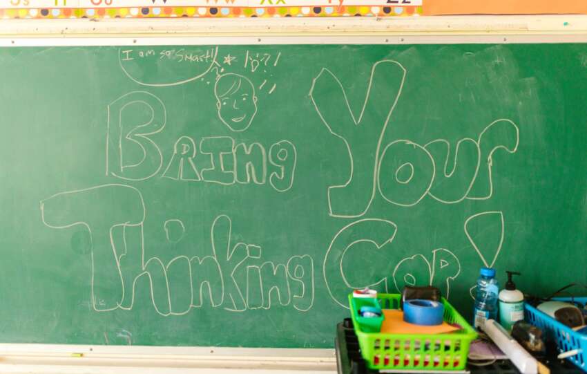 Classroom scene with chalkboard message "Bring Your Thinking Cap" and supplies.